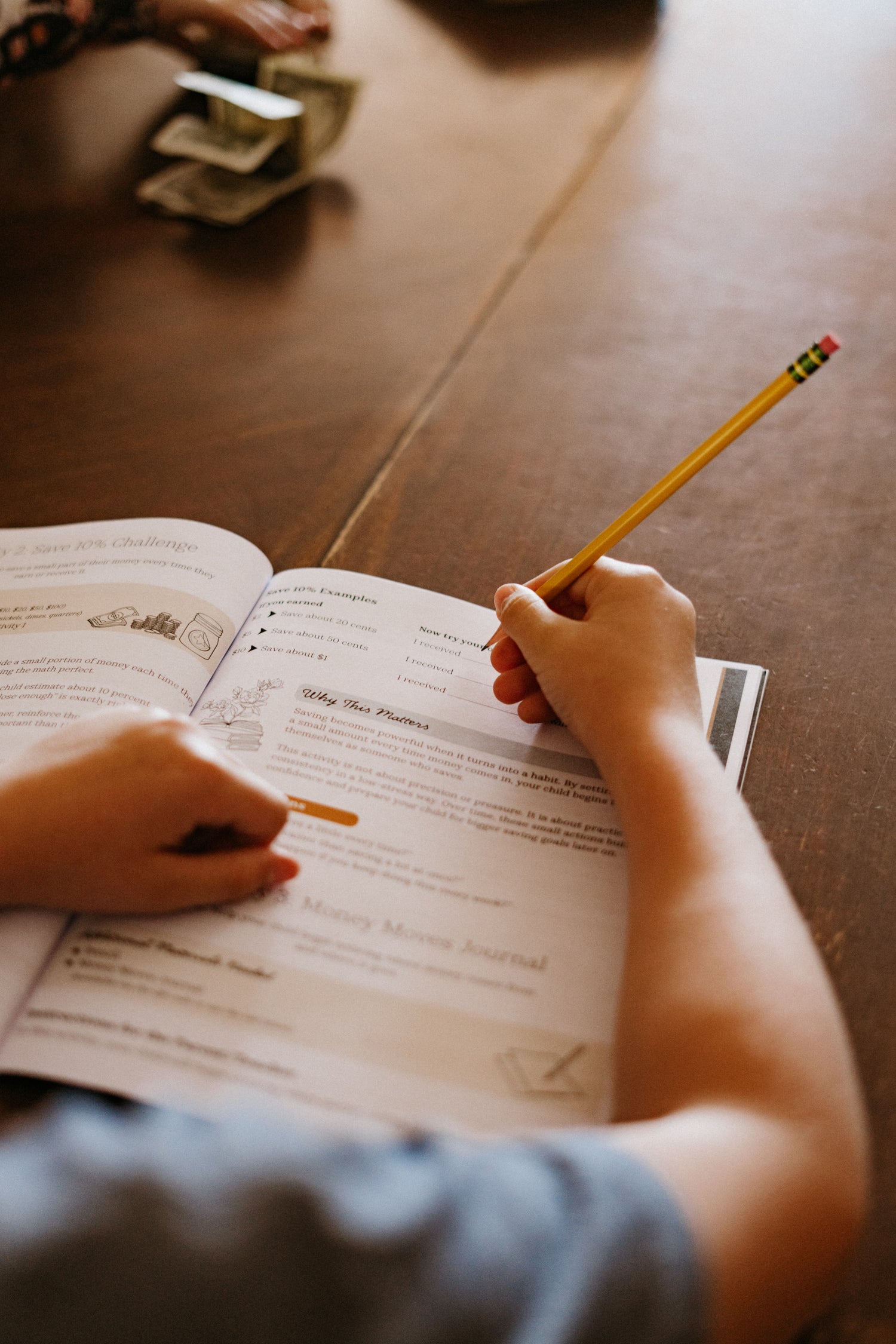 Child writing in a notebook with a pencil on a wooden surface