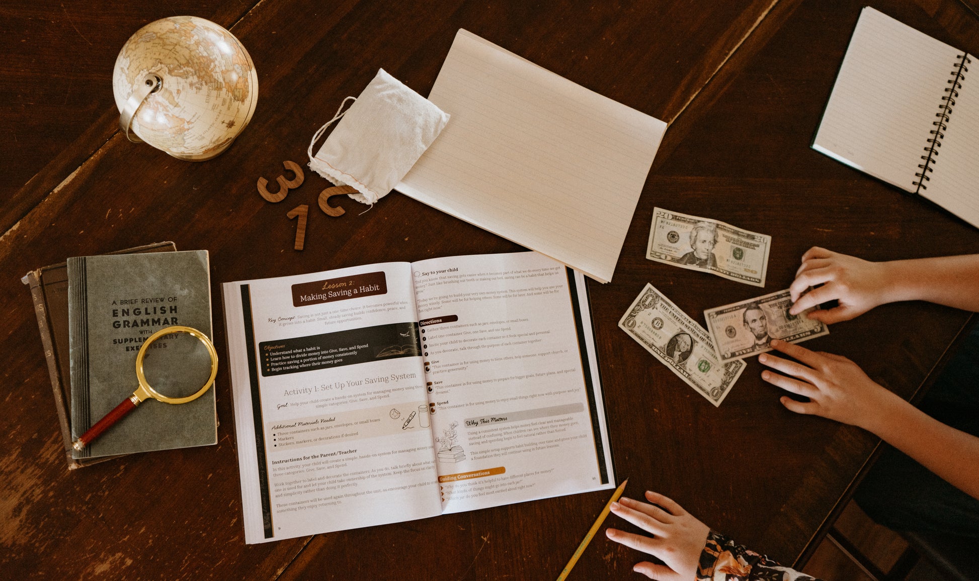 Child counting money on a desk with educational materials and a globe.